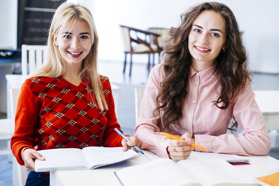 Dwie uśmiechnięte studentki przy stole z podręcznikami