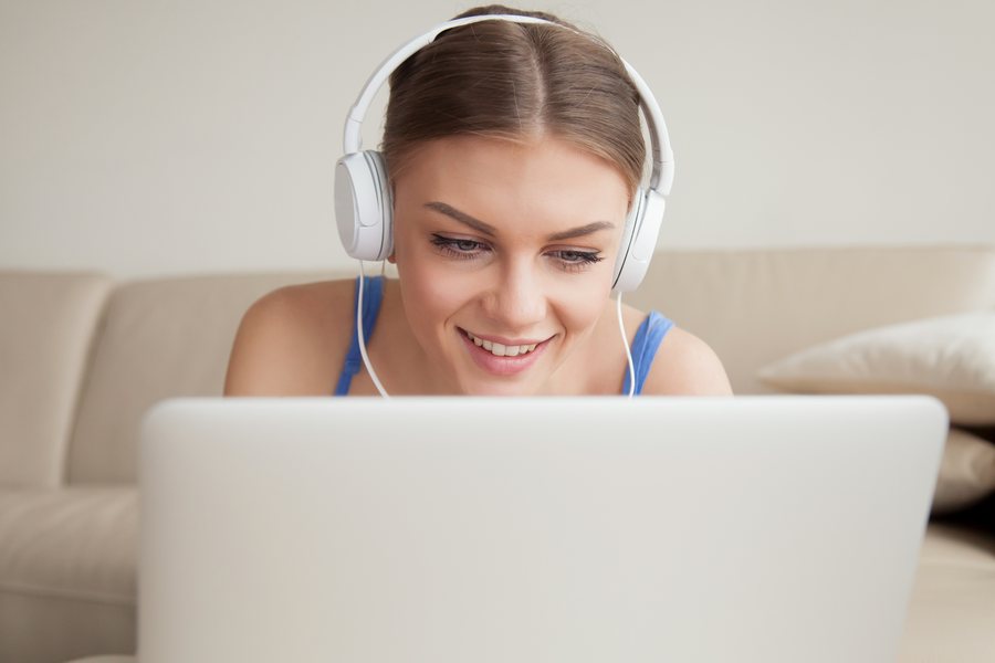 Uśmiechnięta studentka w słuchawkach uczy się przy laptopie